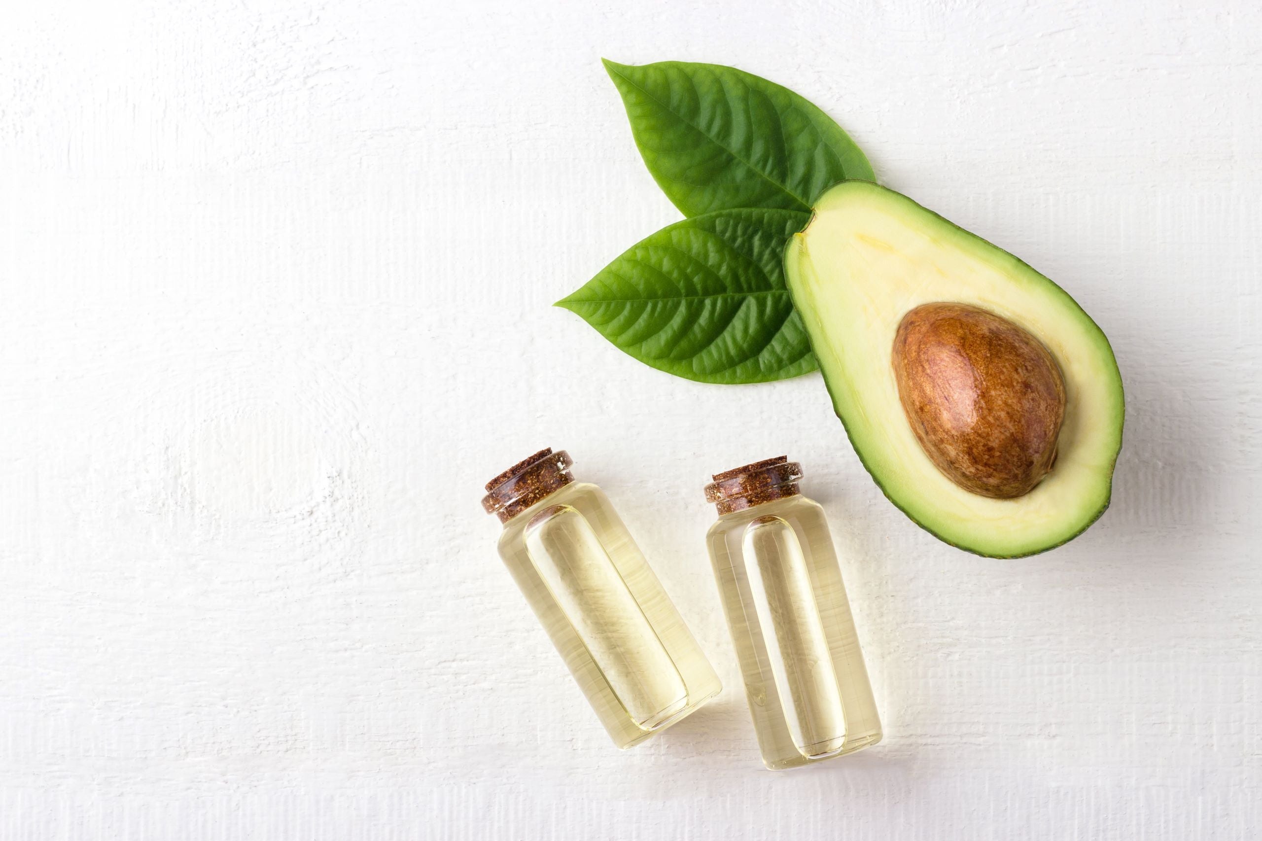 A halved avocado fruit and leaf with two small vials of oil